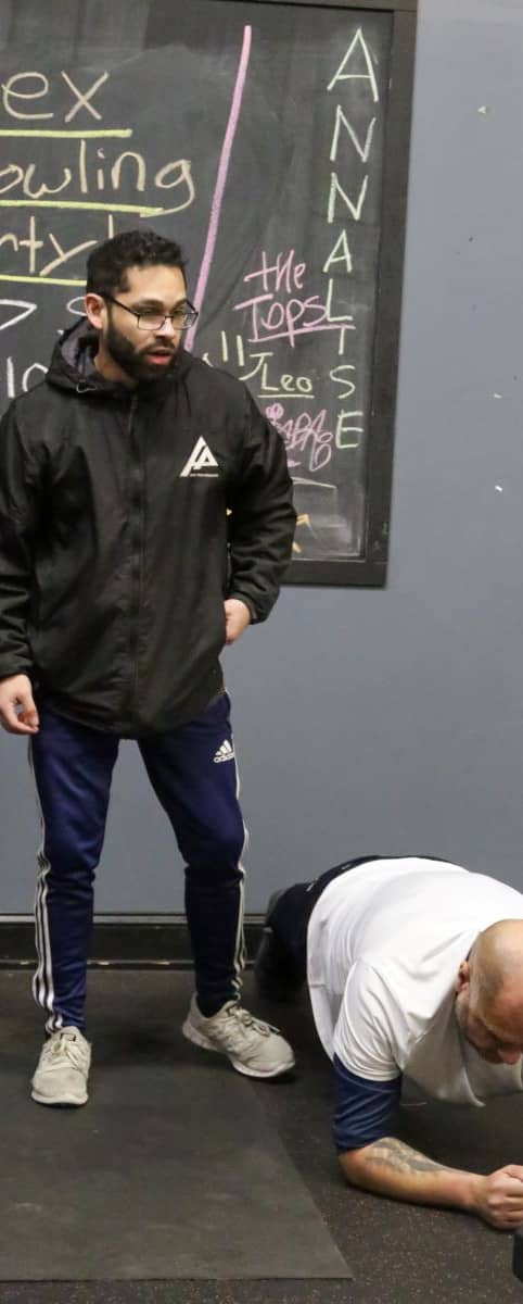 Personal trainer monitors workout near the community event board at Apex Performance Gym, NY.