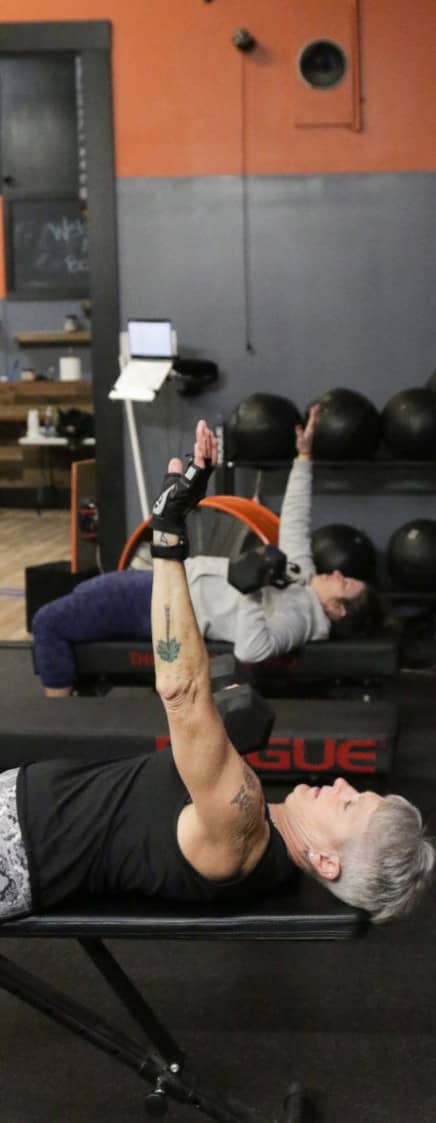Senior gym-goer executes dumbbell chest press at Apex Performance Gym's versatile training space.